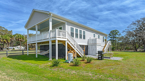 8 Turtle Cottage. A white house on stilts with a yard and blue skies